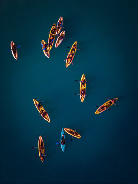 Aerial view of several yellow and blue kayaks with people paddling on deep blue water.