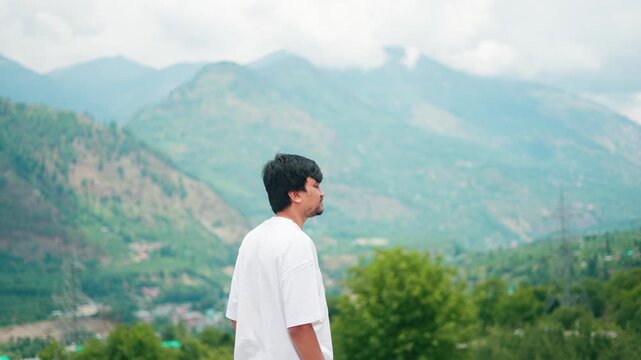 4K Portrait shot of an Indian male tourist walking in front of the Himalayan mountains during the summer season at Manali in Himachal Pradesh, India. Tourist enjoys Himalayas in summer.
