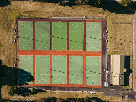 Aerial view of multiple green and red netball courts with white markings and light poles casting long shadows in Devonport, Tasmania, Australia.