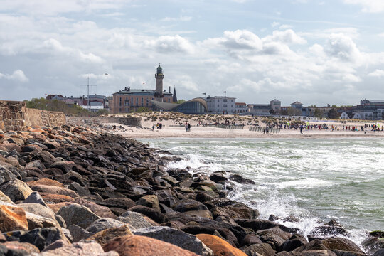 Waves breaking on rocky shoreline in Warnem&uuml;nde with the historic lighthouse and Teepott building visible in the background, Germany