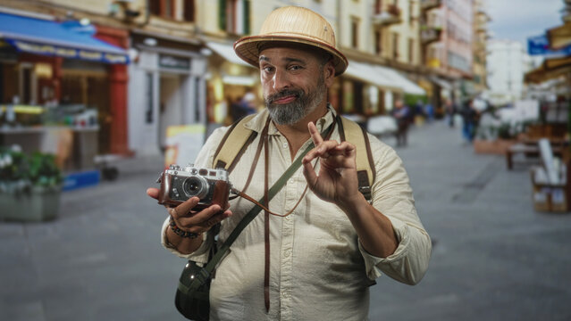 Man holding vintage camera and pointing finger on a street market with backpack and pith helmet visible; curious traveler moment.