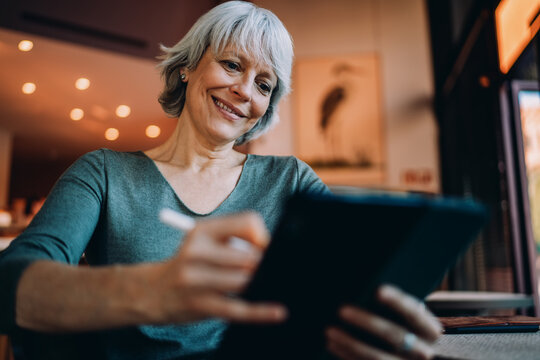 Senior woman focused on digital drawing in tablet, smiling with intent. Represents empowered aging, intuitive creativity and ease with modern mobile technologies.