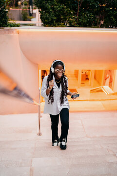 Young woman with vitiligo dancing and laughing while listening to music, happy girl in headphones with smartphone, authentic representation, joy and achievement, carefree digital lifestyle