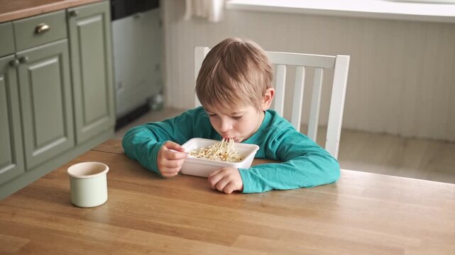 6 years old boy eats instant noodle from box. Child is eating Asian ramen. Lunch time. A good appetite. Tasty children food. Close-up portrait. Carbs dinner. Fast food. Kid eating by himself with fork
