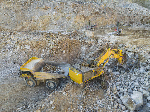 Aerial view of the Santa Lucia de Gordon open-pit quarry with a yellow excavator loading rocks into a dump truck Santa Lucia de Gordon, Castile and Leon, Spain.