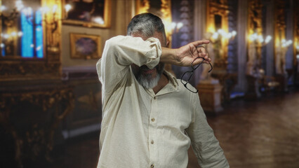 Middle aged man covering face with hand while holding glasses in building museum gallery  privacy avoidance embarrassment. © Krakenimages.com