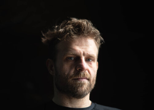 Pensive thoughtful white male portrait on dark background, natural light and shadow, mental health theme, 