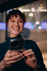 Fototapeta premium Laughing young woman with freckles holds smartphone, captured in a joyful candid moment, symbolizing emotional connection and digital spontaneity in modern urban life.