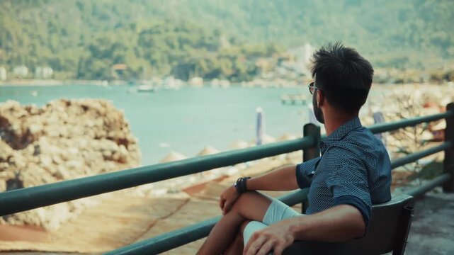 Man Sitting On Terrace And Looking At Sea Bay. Traveler Relaxing During Vacation At Resort