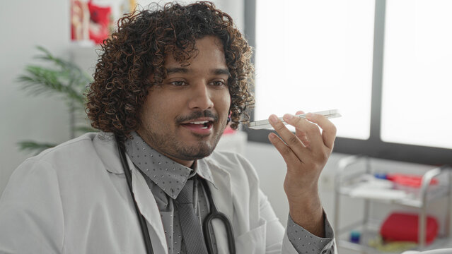 Young doctor man speaking into smartphone, holding phone to mouth, hand raised, in clinic building; compassionate care.