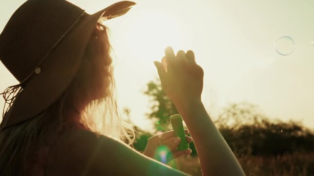 Woman Blowing Soap Bubbles At Sunset In Summer Meadow. Vacation And Joyful Moment