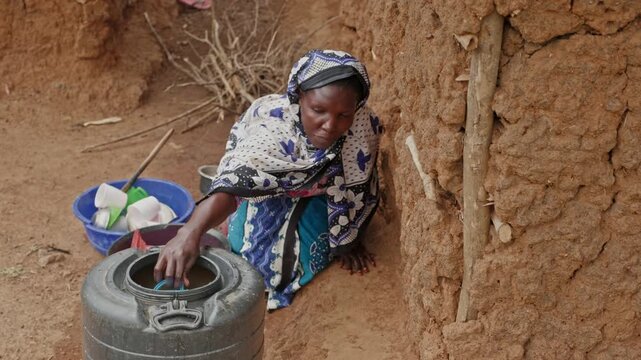 Close-up of a woman collecting water with a cup from a storage container in rural Africa. The scene highlights water scarcity, unsafe water conditions, and the essential need for clean water in daily 