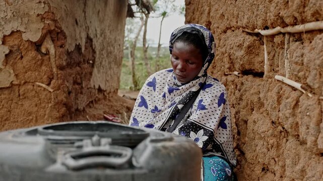 Close-up of a woman collecting water with a cup from a storage container in rural Africa. The scene highlights water scarcity, unsafe water conditions, and the essential need for clean water in daily 