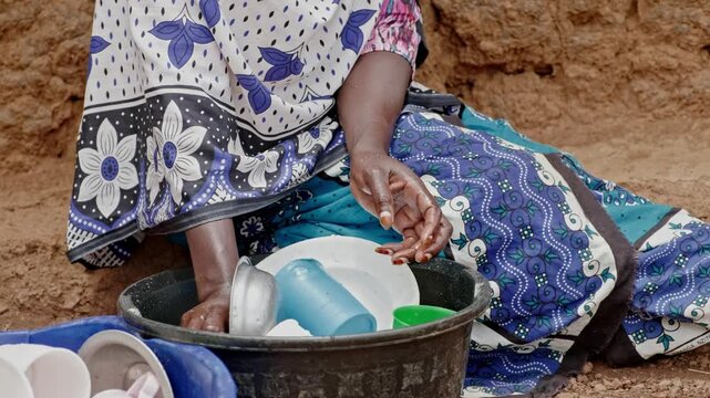 Close-up of hands washing dishes with limited water in rural Africa. The scene highlights water scarcity, hygiene challenges, and the importance of clean water for daily life and health.