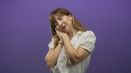 Fototapeta premium Woman resting head on hands with closed eyes and relaxed expression in a purple studio setting wearing white blouse; calm rest.