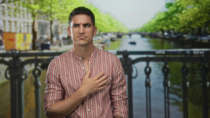 Fototapeta premium Man clutching chest for heartattack on street in amsterdam by canal bridge, striped shirt visible; pain vulnerability.