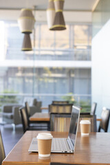 Open silver laptop sitting on wooden table with paper coffee cup near glass wall © wavebreak3