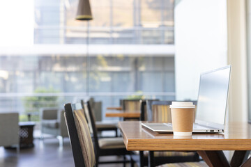 Paper coffee cup sitting on wooden table beside slim laptop at modern cafe, copy space © wavebreak3