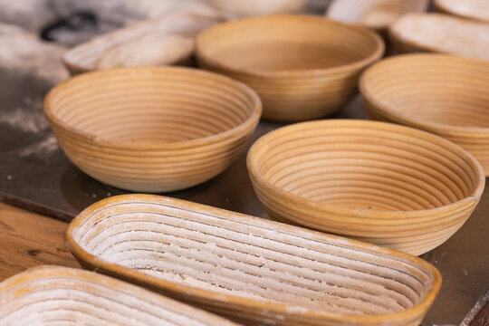 Coiled rattan bannetons sitting on wooden bench in bakery, showing flour dusting grooves