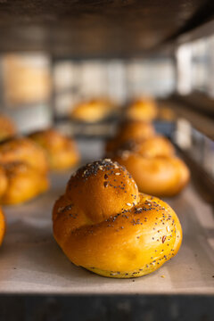 Golden knot roll resting on parchment-lined metal tray on bakery rack, gleaming with poppy seeds