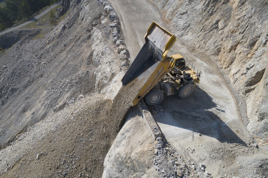 Aerial view of a large yellow dump truck unloading rocks at an open-pit mine on a steep rocky slope in Santa Lucia de Gordon, Castile and Leon, Spain.