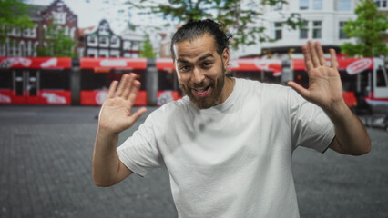 Naklejka premium Man with hands raised palms up wearing white t shirt on a cobbled city street in front of tram and shops, waving openly; friendly greeting happy.