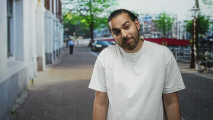Fototapeta premium Man with beard and bun wearing white t shirt standing on street smiling at camera; relaxed confidence.