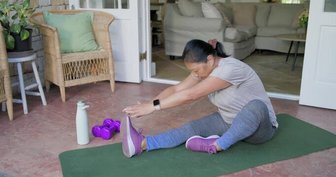Senior Asian woman is starting by reaching toward toes on green mat on porch improving mobility