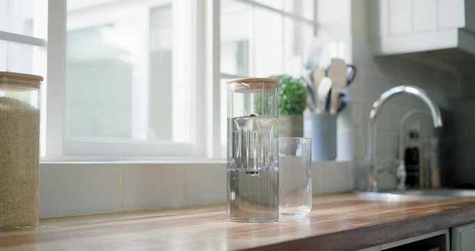 Tall carafe and glass sitting on wooden counter, water being poured off-frame for kitchen styling