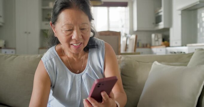 Senior Asian woman after ping tapping pink smartphone, sipping mug, reading reacting in living room