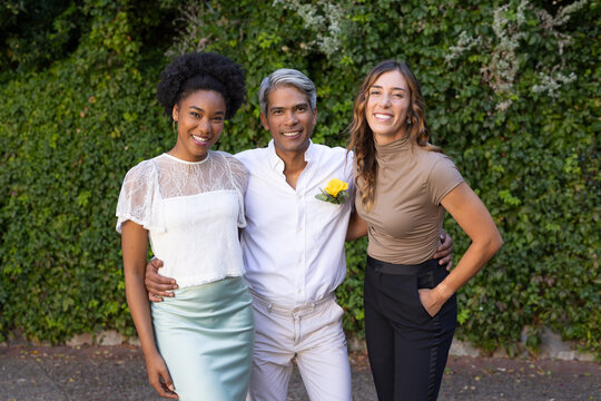 Diverse friends standing with linked arms by ivy wall, man wearing white shirt and boutonniere