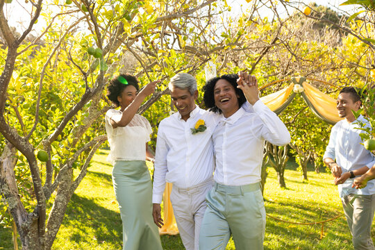 African American couple walking grove aisle under arch in white with boutonniere tossing petals