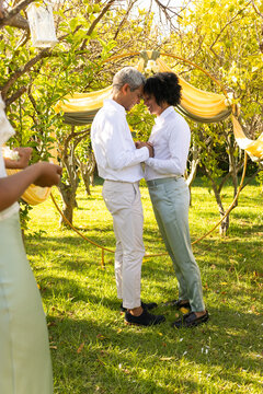 African American couple exchanging vows beneath circular hoop arch draped yellow fabric in orchard