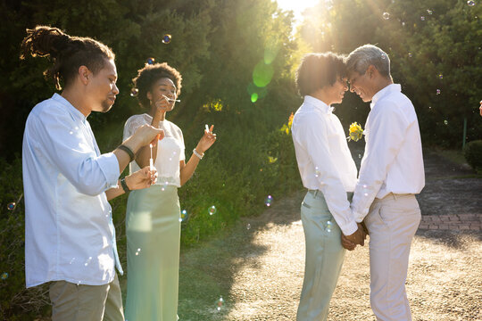 African American couple holding hands, touching foreheads on sunlit path with soap bubbles