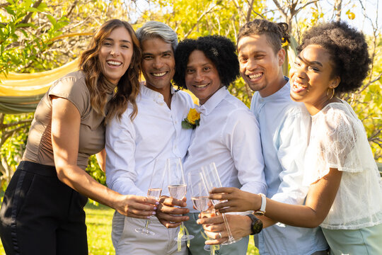 Diverse friends raising champagne flutes and toasting in sunlit garden with yellow boutonniere
