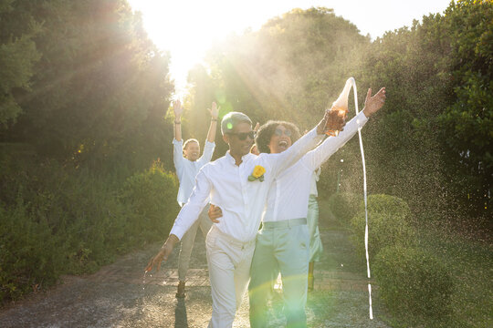 African American friends walking garden path wearing white shirts, pouring from bottle