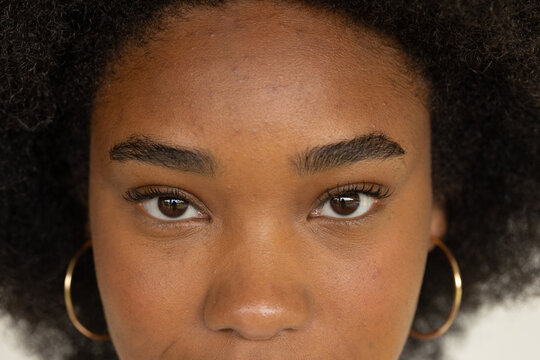 African adult female facing camera against neutral backdrop, showing gold hoop earrings and texture