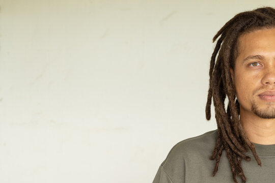African American male posing on right by offwhite wall with dreads and green crewneck, copy space