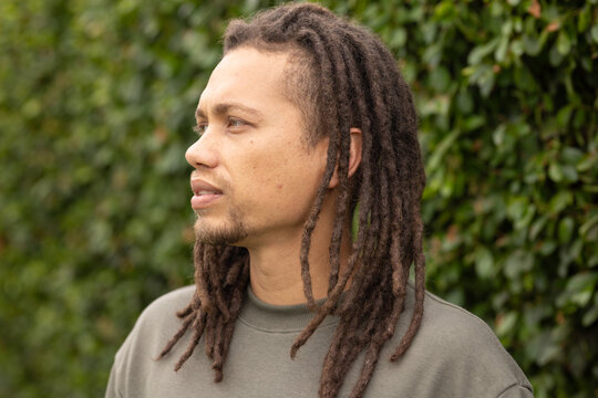 Mid-adult African American man standing and looking left by green hedge wearing olive sweatshirt