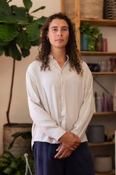 African American non-binary person standing centered in studio with fiddle-leaf plant and shelving