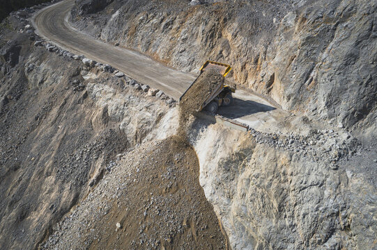 Aerial view of a yellow dump truck unloading earth and rocks on a steep hillside at an open-pit mine in Santa Lucia de Gordon, Castile and Leon, Spain.