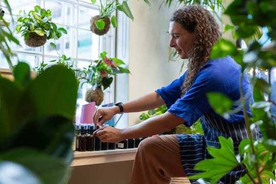African American non-binary in striped apron sitting on sill arranging amber bottles, copy space