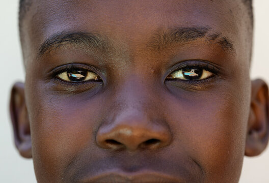African American male youth gazing at camera against plain wall, showing camera reflection in eyes