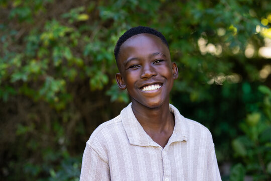 Adolescent African male smiling while standing facing camera in garden wearing beige collared shirt