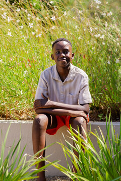 Youth male sitting on concrete planter edge in garden with ornamental grasses, wearing light shirt