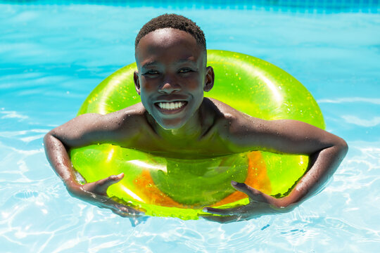 Male teenager smiling while floating chest-deep in swimming pool on lime-green glitter ring