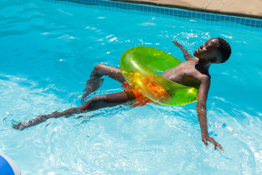 African American youth male floating in green ring, reclining in pool wearing orange trunks
