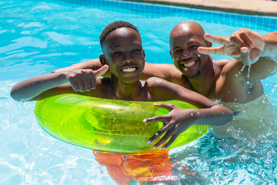 African American dad and youth smiling in shallow pool with green tube youth wearing orange trunks