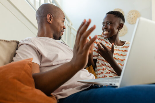 Vertical video: African American father and teen son reacting to laptop, laughing on sofa at home