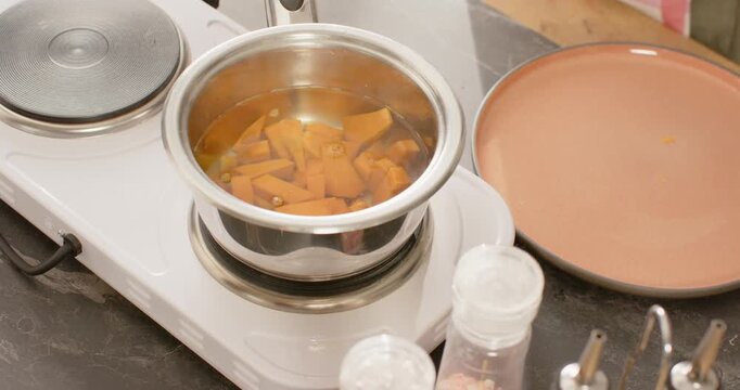 Metal pot with chopped carrots is simmering on hotplate as burner is heating for plating